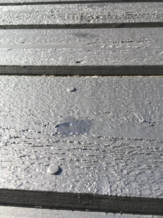 Målad träfasad med synliga ändskarvar och sprickbildning, samt spikar och vattendroppar efter regn.