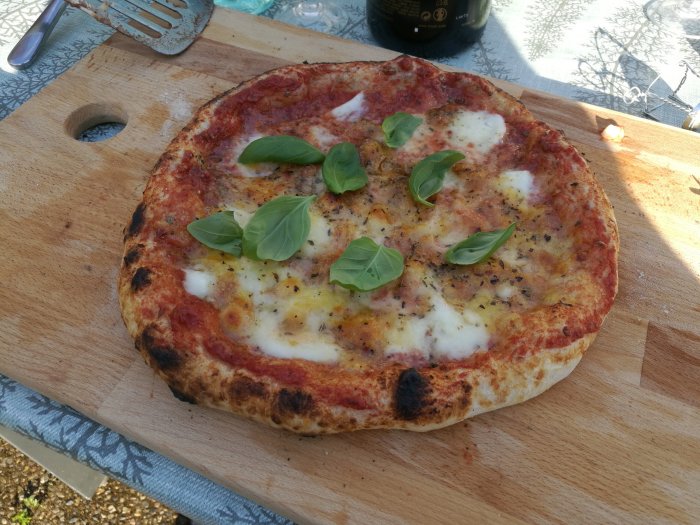 Hemgjord pizza med tomatsås, ost och basilikablad på träskärbräda.