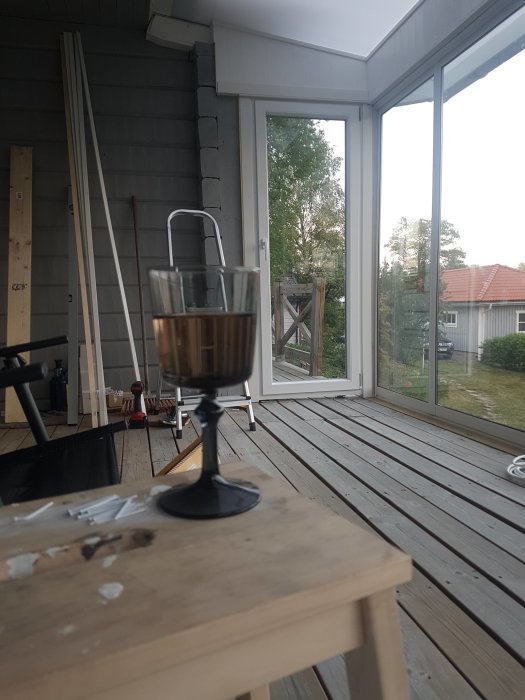 Ett glas rosévin på ett arbetsbord på en veranda med nyinstallerad dörr och fönster i bakgrunden.