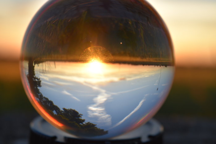 Solnedgång speglad i en kristallkula med träd och himmel.