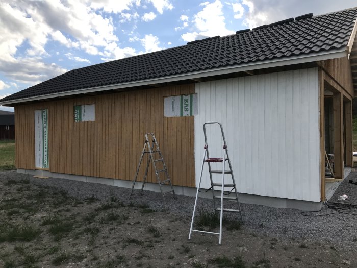 Halvmålad träfasad på ett hus med öppna fönsterutskärningar och en stege lutad mot väggen.