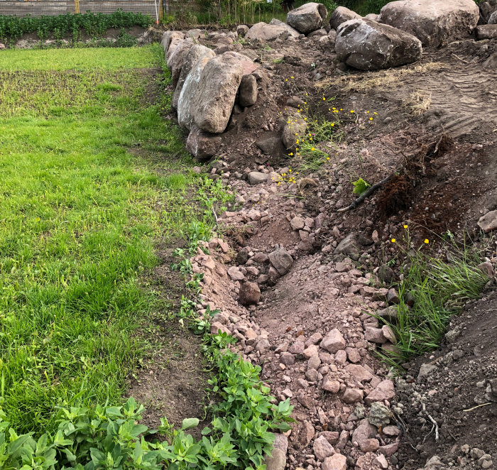 Stor stenmur under konstruktion vid en tomtgräns, stenar står på ändan utan dränering.