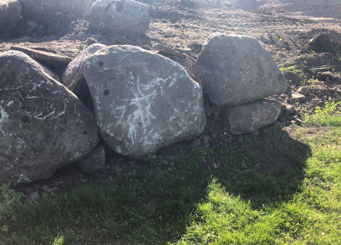 Stora stenar staplade i en oregelbunden hög som ska utgöra en stödmur, med synlig grusgrund.