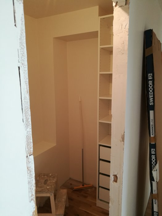 Öppning till en klädkammare under renovering, med oslipat och omålat väggparti och omonterad PAX garderob.