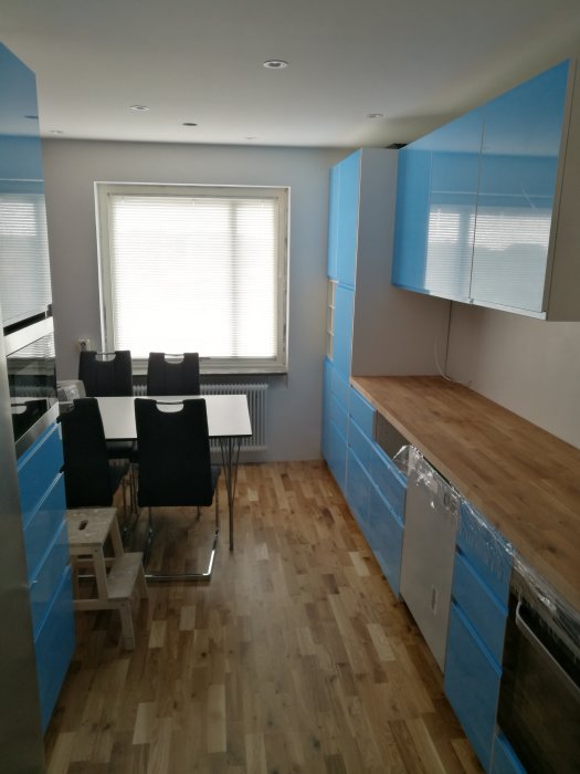 Kök under renovering med blå köksskåp, ekparkett och matplats framför fönstret.