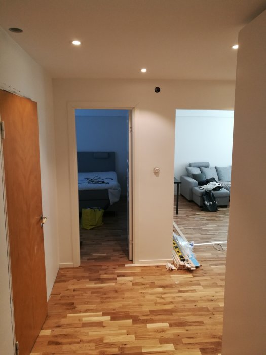 Nyinstallerat ekparkettgolv och vitmålade väggar i en lägenhet under renovering med öppna dörrar till sovrum och vardagsrum.