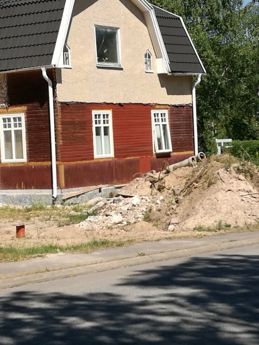 Delvis renoverat hus där putsen tagits ner för att visa ursprungliga material, med byggavfall framför.