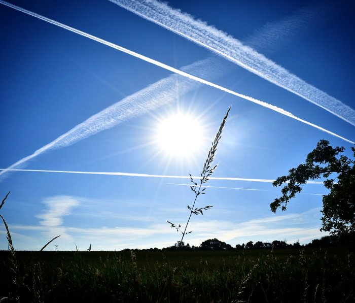 Solig himmel över fält med flygplansstrimmor i Skåne och en klar sol.