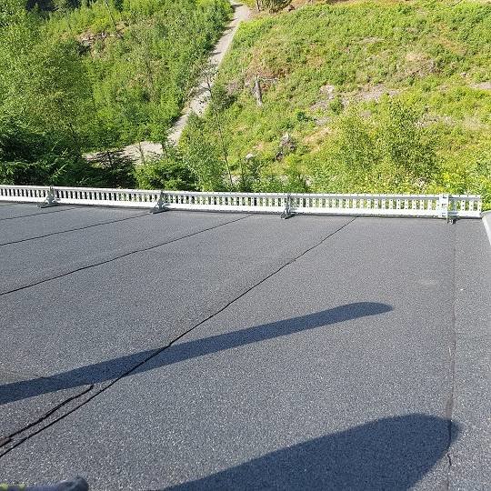 Svart takpapp på gäststugans tak med oanvänd takgenomföring och skugga av person.