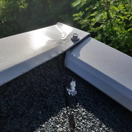 Detaljbild på taket med fokus på en skarv där takpappen möter en metallkant, synliga tecken på läckage.