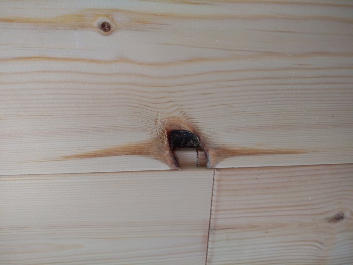 Träpanel med en stor knothålsskada som exponerar det mörka insidan.