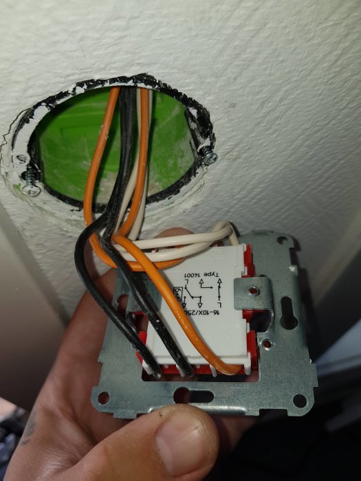 Hand som håller en elektrisk brytare med oskyddade elkablar inför installation i en väggdosa.