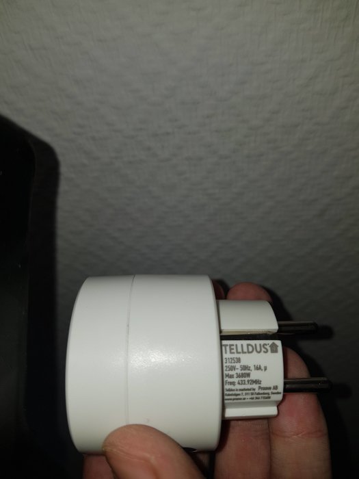Hand håller en Telldus smart plug för att styra lampor i hemmet trådlöst.