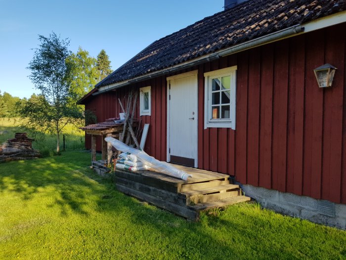 Nybyggd trappa av trä utanför en rödmålad uthusbyggnad med vita knutar.