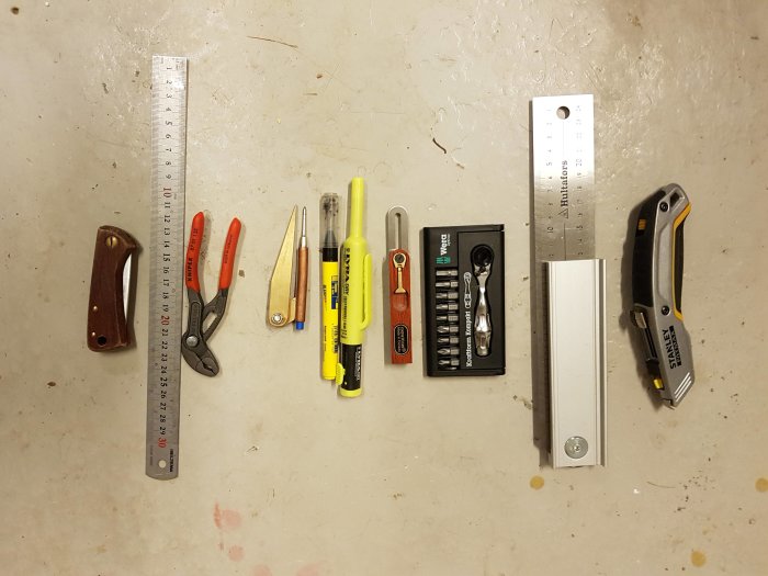 Verktyg för båtrenovering ordnade på golv: kniv, skruvmejslar, pennor, tång, måttband och bitsats.