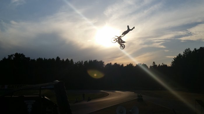 Motocrossförare utför ett stunt i luften mot en solnedgångshimmel.