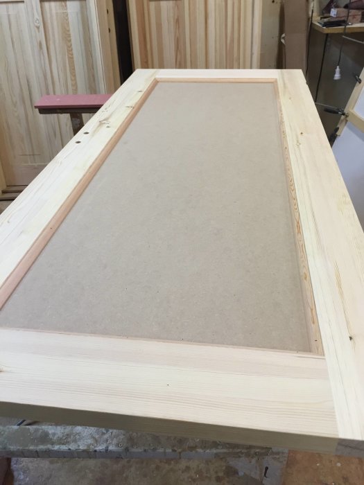 En obehandlad badrumsdörr av Oregon pine trä med lister och en infälld Tricoya MDF-panel, under konstruktion i en verkstad.