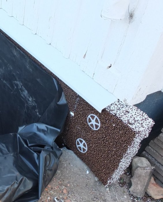 Delvis isolerad källarvägg med dräneringsplattor, gummiduk och dropplist vid grundens kant.