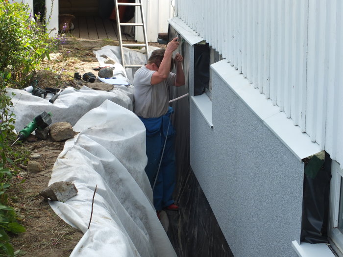 Person som installerar isolering på husgrund med markduk och isoleringsmaterial synligt.