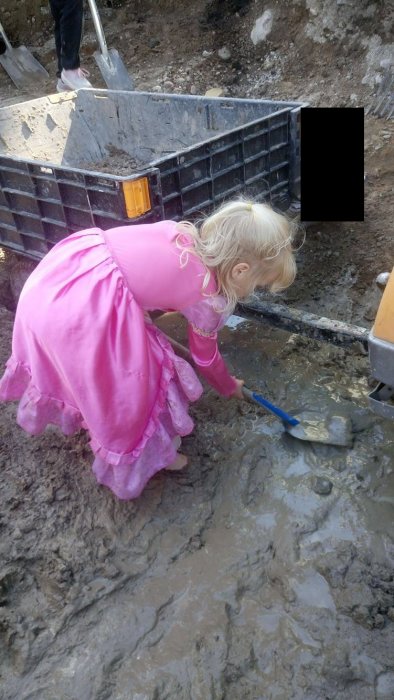 Barn i rosa klänning hjälper till att gräva i lerig mark med en spade.