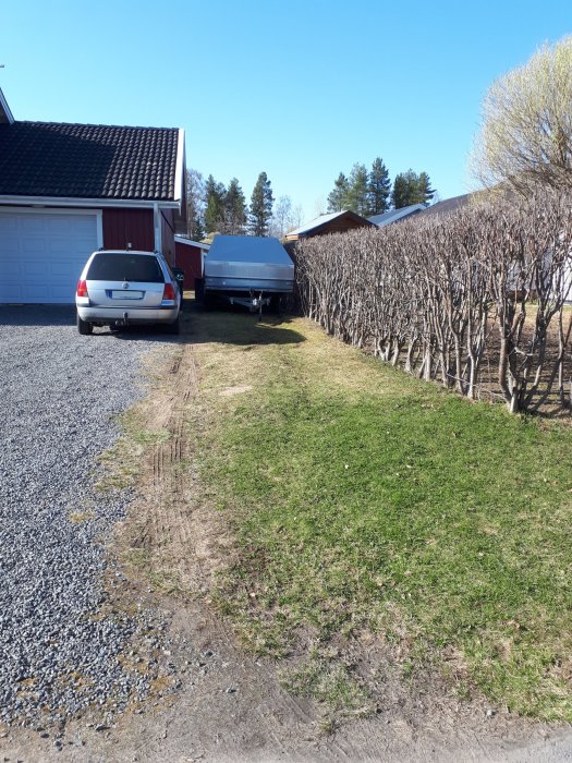 Grusinfart med bil och släpvagn bredvid rönnhäck, planer för att bredda för bättre parkering.