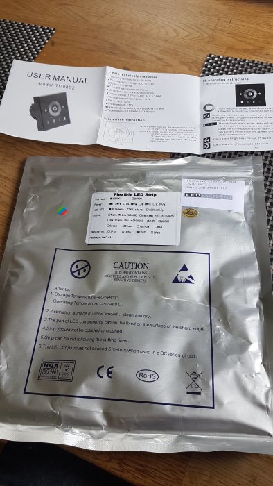 Anvisningshäfte för RGB-kontroller och förpackad flexibel LED-strip på ett bord.