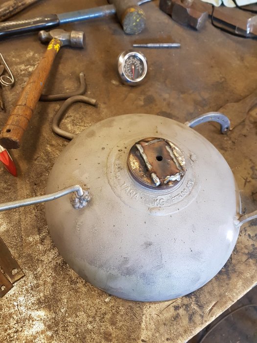 Värmepanna på en arbetsbänk omgiven av verktyg inklusive en hammare, skiftnyckel och avläsbar termometer.