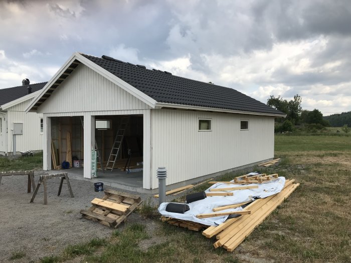 Nybyggt hus med färdigmålade väggar och monterade fönster, byggmaterial i förgrunden.