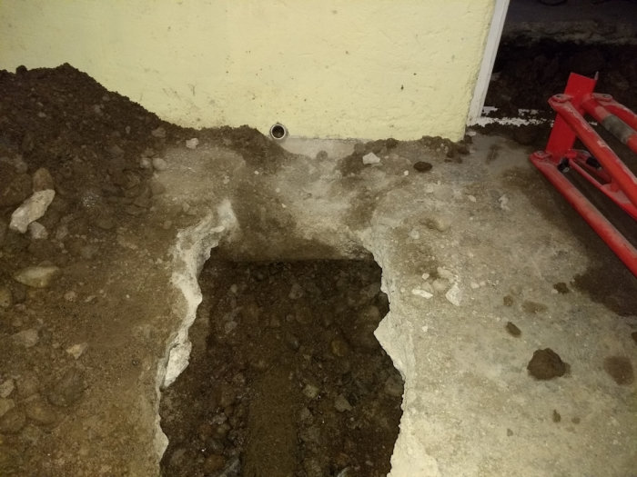 Vattenansamling under husets grund med synligt rostigt rör och uppbruten betongplatta.