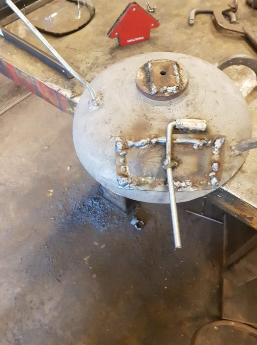 Svetsad metallkonstruktion med bultar och stag på en verkstadsbänk.