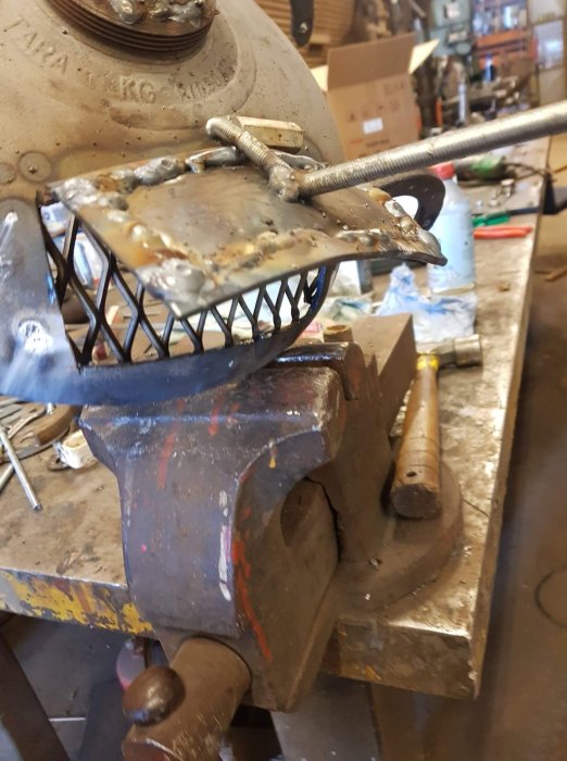 Svetsning av metallram i skruvstäd på arbetsbänk.