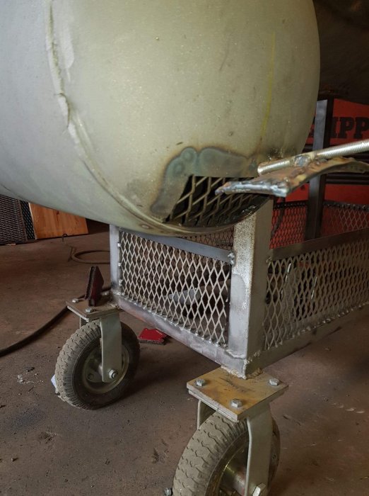 Bild av en betongblandare på hjul med synliga svetsfogar och en stålnät-korg i ett garage.