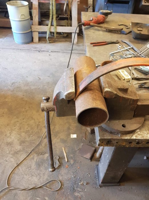 Skrivbänk med fastklämd metallrör och verktyg i en smedja.