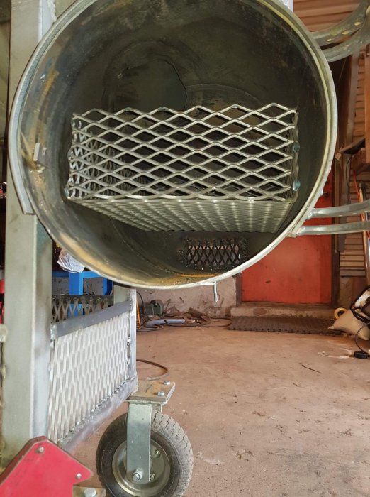 Bild på ett metallgaller monterat inuti en trumliknande konstruktion på en verkstad.