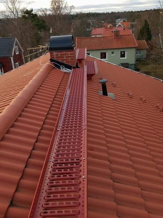 Takbrygga installerad på ett rött tegeltak med omgivande hus och träd i bakgrunden.