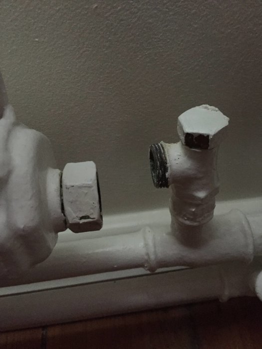 Målad radiatoranslutning med synliga gipsade rör och kopplingar mot vägg.
