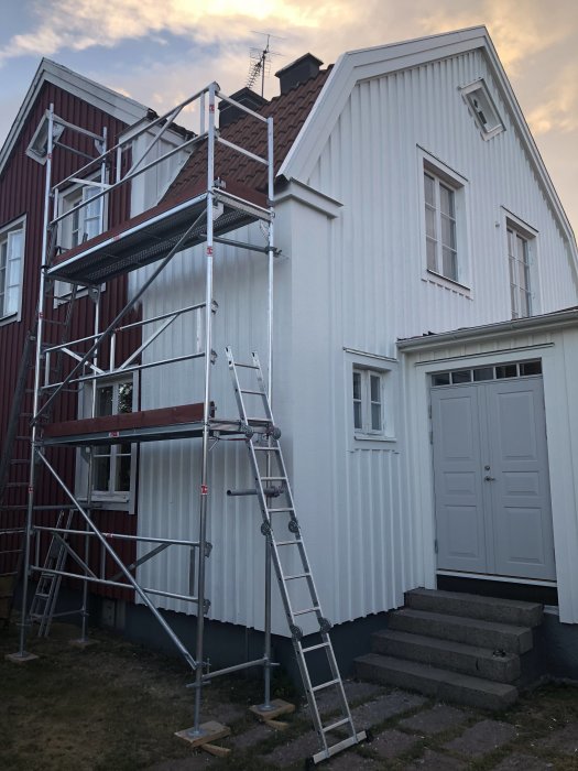 Ställning vid vitmålad hörna av hus med röda och vita fasader under renovering.