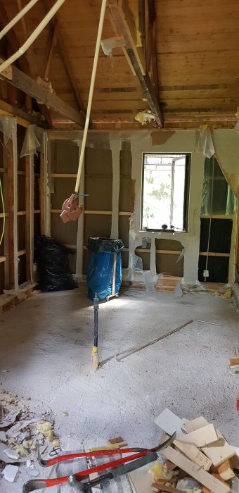 Rivningsarbete inuti ett hus med synligt träbjälklag, upprivet golv och väggar, samt byggverktyg och materialrester.