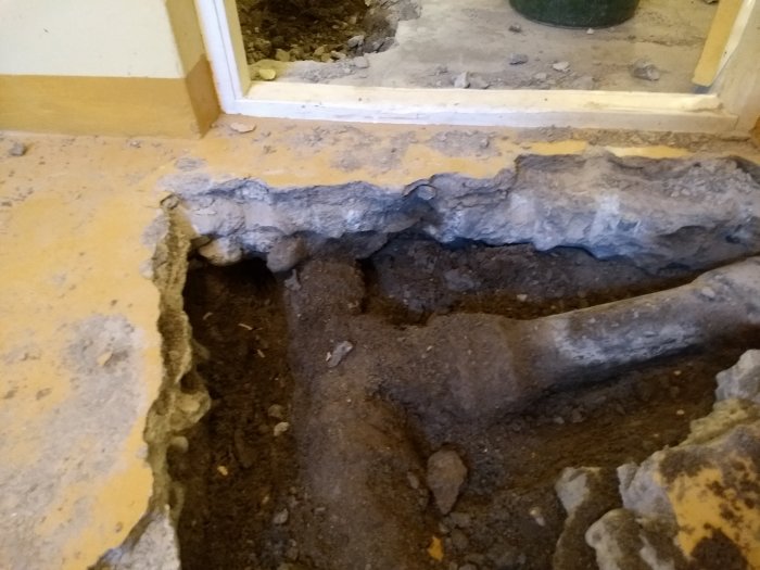 Uppbruten betongsockel i ett hus med synlig armering och ett rör som ligger an mot sockeln.