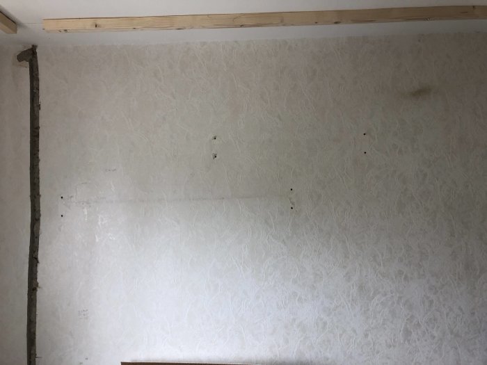 Vägg med delvis borttagen tapet och frästa kanaler, redo för renovering.