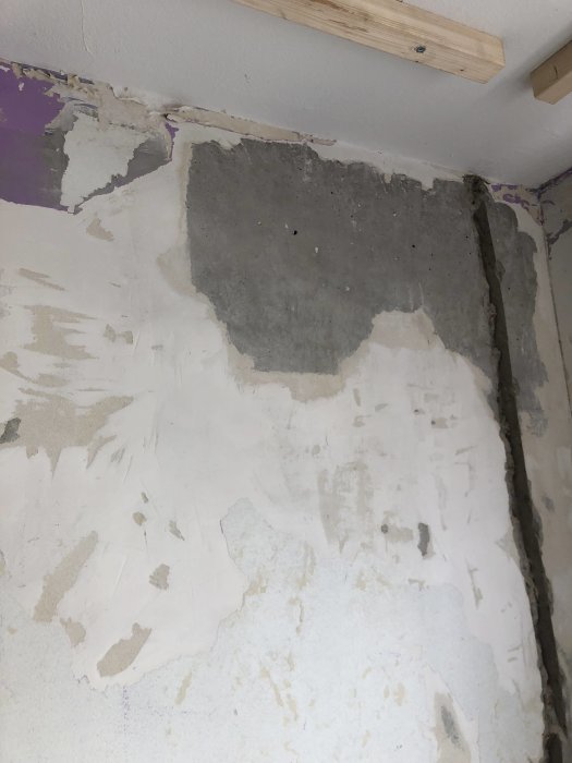 Betongvägg med frästa kanaler för elledningar och områden där tapeter avlägsnats, visande lager av material.