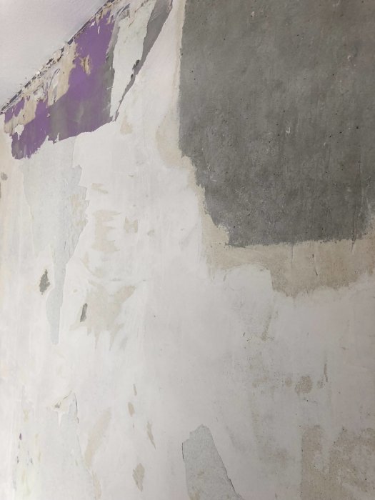 Delvis renoverad vägg med lager av betong, spackel och rester av tapet och färg.