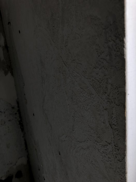 Betongvägg med frästa kanaler för eldragning, delvis borttagen puts och spackel samt en synlig hörndetalj.