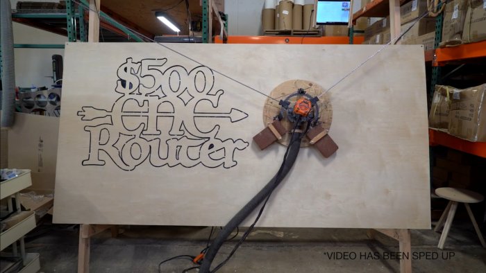 Plywoodskiva med utskuren text "$500 CNC Router" genom Maslow CNC-maskin i en verkstad.