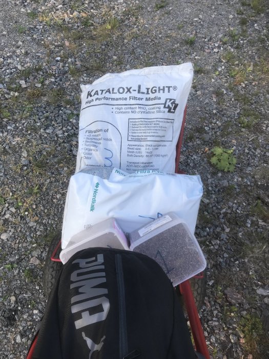 Filtermedia Katalox-Light i förpackning på marken bredvid ryggsäck och byggmaterial.