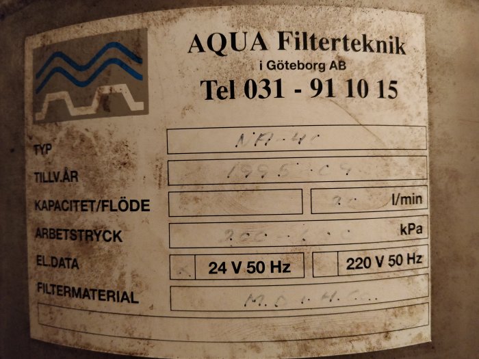 Gamla vattenfilteretiketten med delvis oläslig text och logotyp, indikerar modell NA-4C och material MD+HCo.