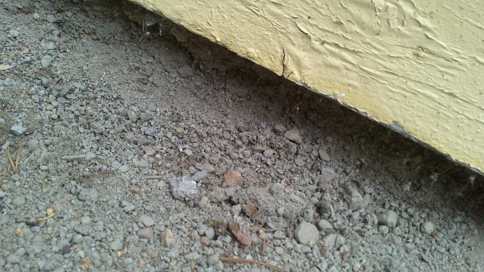 Hål inunder kanten på ett hus, utan synlig grund, upptäckt efter borttagning av stenplattor.