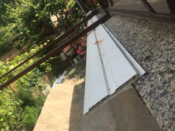Hvide plastpaneler liggende på en betonoverflade i en have med planter i baggrunden.