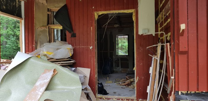 Renoveringsarbete där råspont sågats bort och ytterdörren flyttats, med synlig isolering och byggavfall.