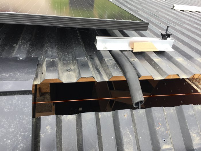 Solpanelkabel dras genom tjock gummislang längs "dal" på plåttak för elinstallation.